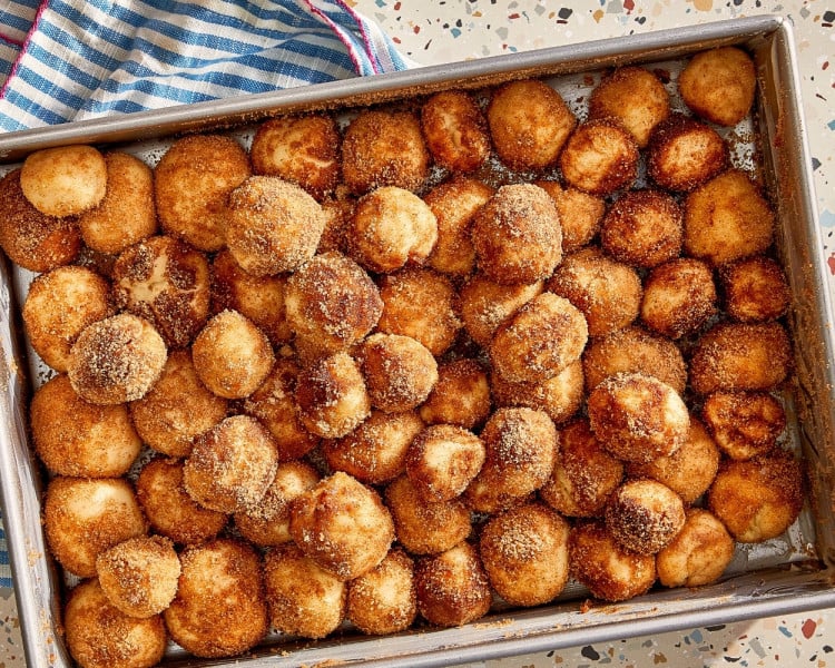 Cinnamon sugar-coated cinnamon roll bites arranged snugly in a greased baking pan before the second rise.