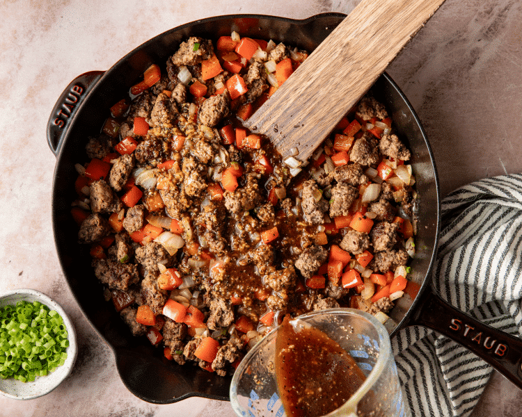 Pouring sauce over cooked beef and vegetables.