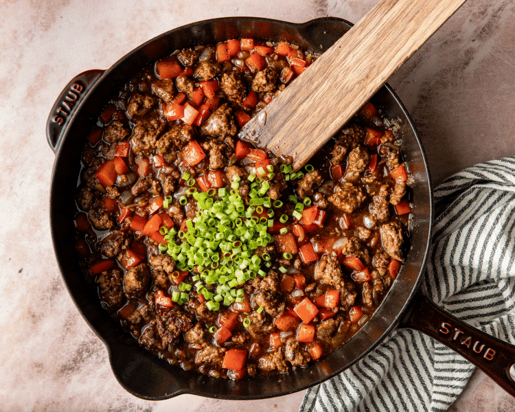 Adding green onions to finished honey garlic beef skillet.