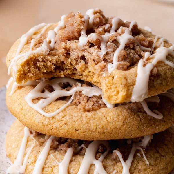 Three pumpkin coffee cake cookies stacked on top of each other with the top cookie having a bite taken out of it.