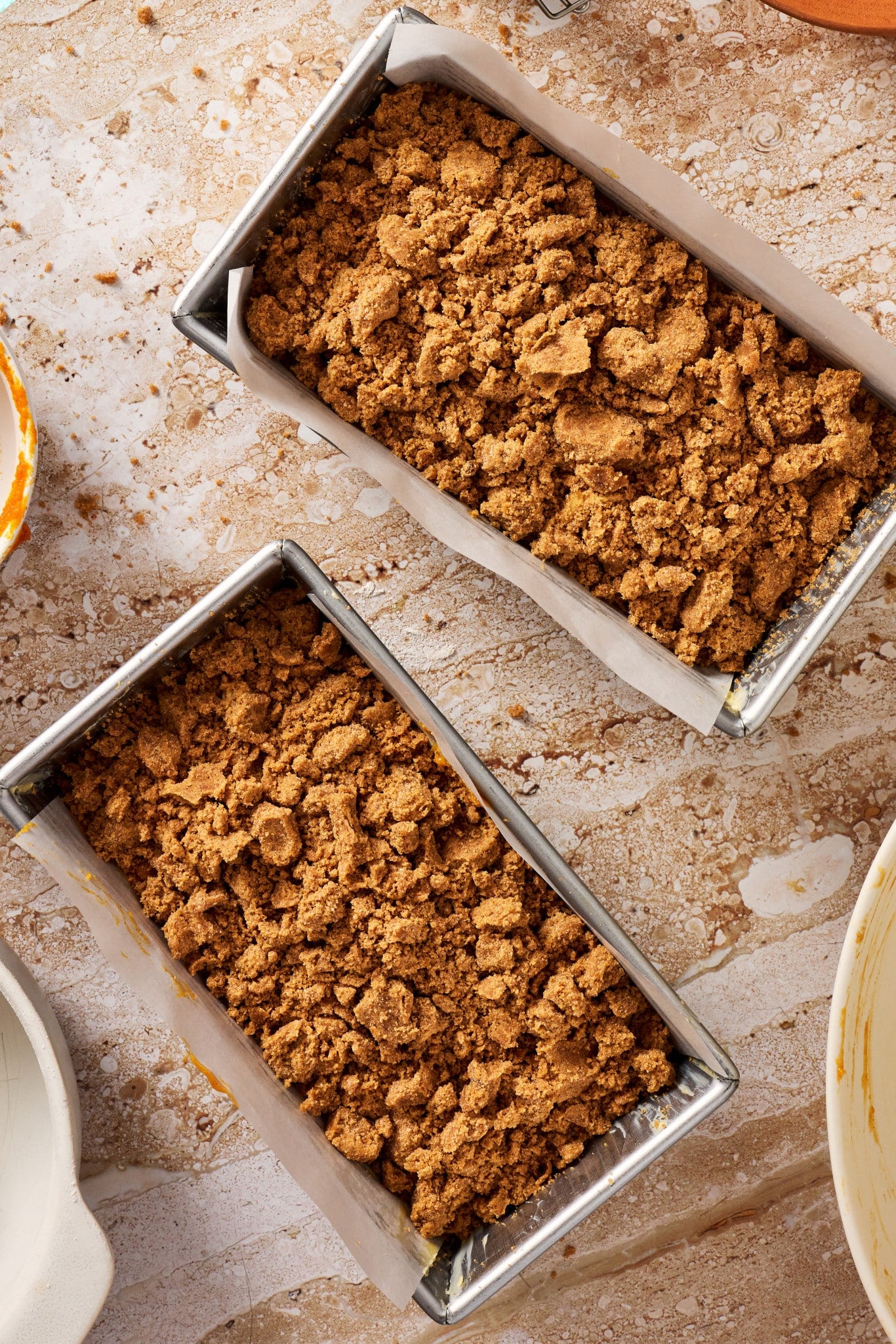 Two loaf pans filled with pumpkin bread batter and generously topped with pumpkin spice streusel before baking.