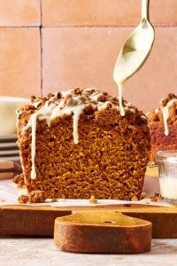 Freshly baked Pumpkin Streusel Bread topped with buttery brown sugar streusel as vanilla glaze is drizzled over the loaf.