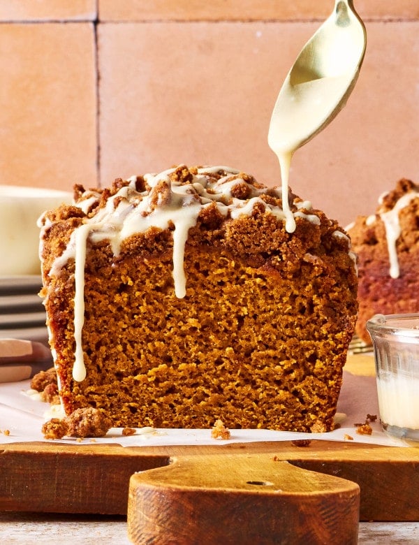 Freshly baked Pumpkin Streusel Bread topped with buttery brown sugar streusel as vanilla glaze is drizzled over the loaf.