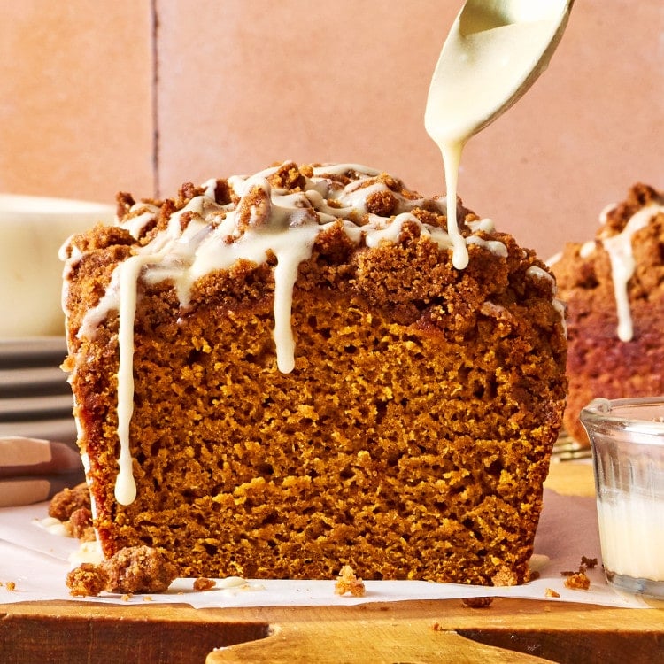 Freshly baked Pumpkin Streusel Bread topped with buttery brown sugar streusel as vanilla glaze is drizzled over the loaf.