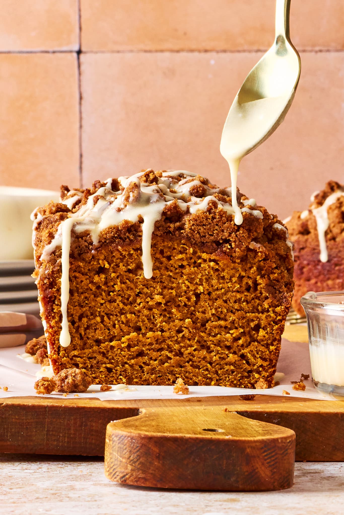 Freshly baked Pumpkin Streusel Bread topped with buttery brown sugar streusel as vanilla glaze is drizzled over the loaf.