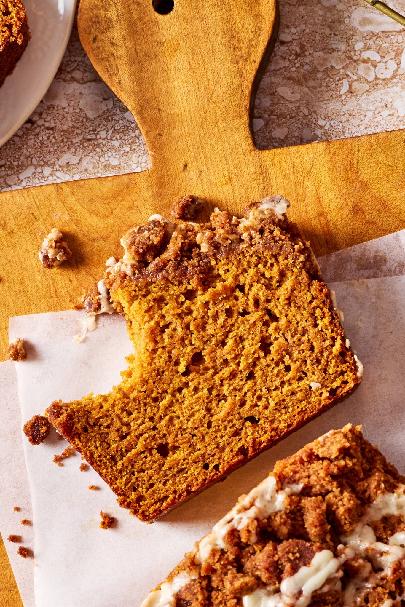 Slice of moist Pumpkin Streusel Bread on a wooden serving board with pumpkin spice streusel and vanilla glaze on top.