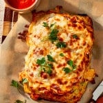 Chicken parmesan meatloaf baked and resting on parchment lined baking sheet and garnished with fresh parsley.