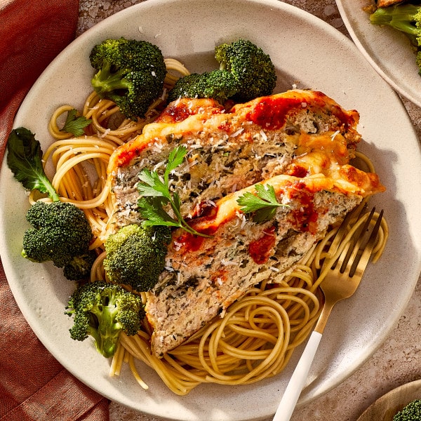 Two slices of chicken parmesan meatloaf served on top of spaghetti and broccoli.