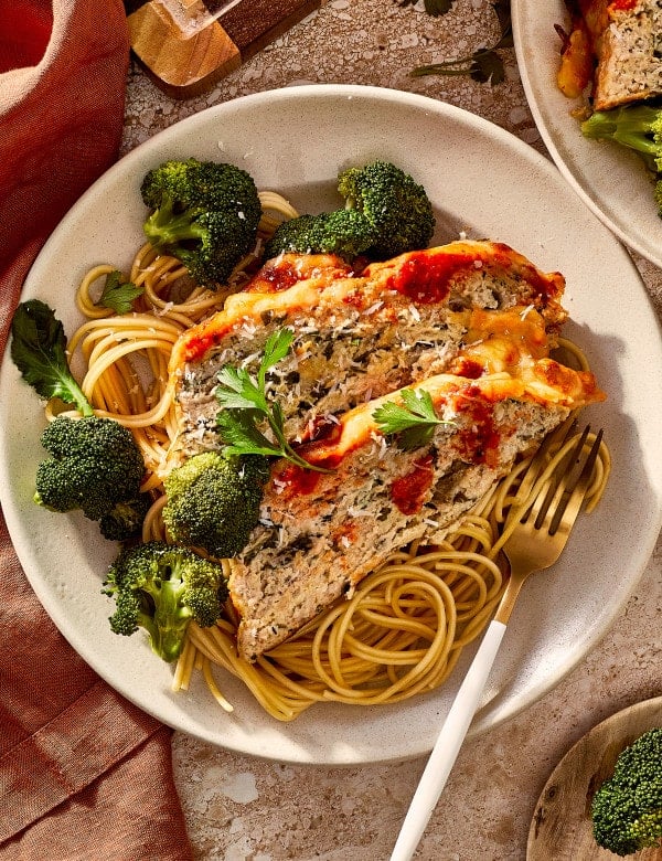 Two slices of chicken parmesan meatloaf served on top of spaghetti and broccoli.