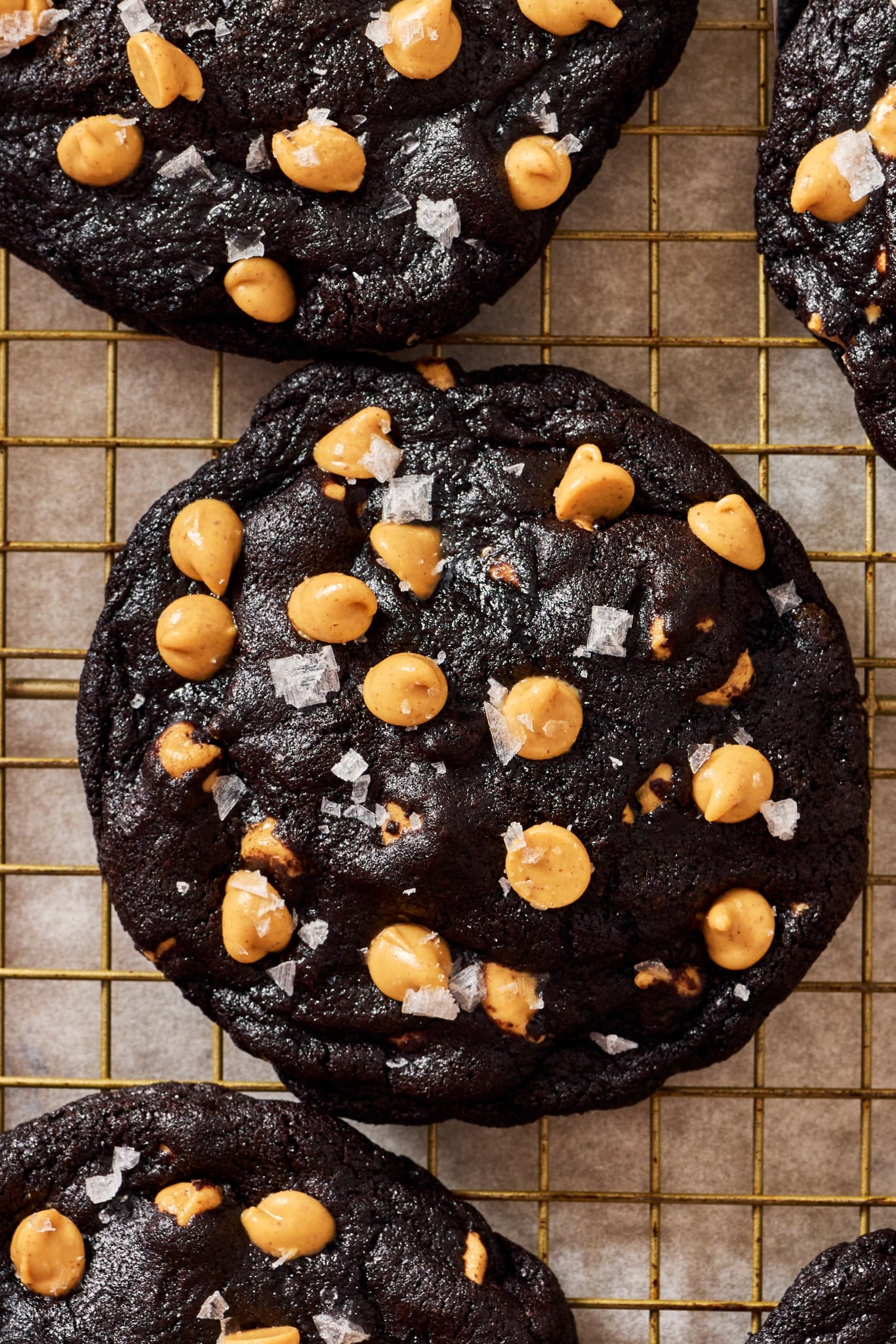 Chocolate peanut butter chip cookie sprinkled with flaky sea salt cooling on wire rack.