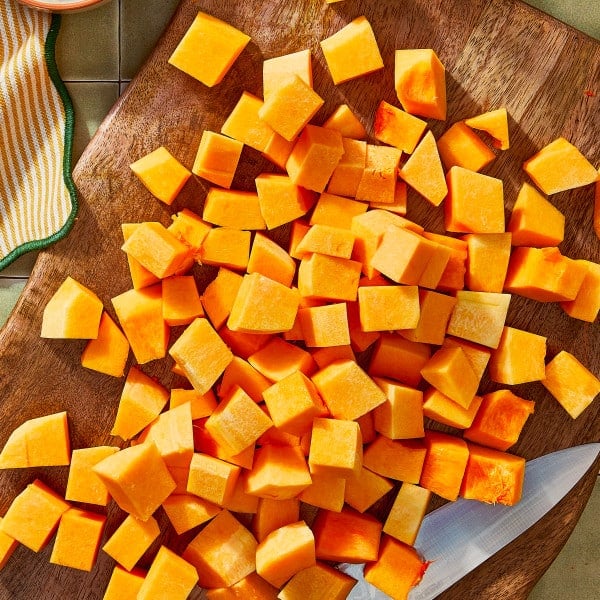 Butternut squash cut into cubes on wooden cutting board.
