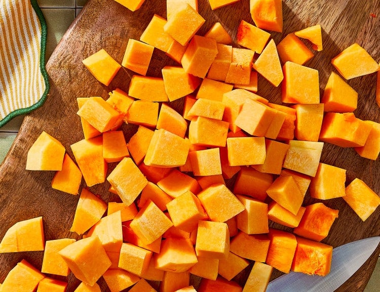Butternut squash cut into cubes on wooden cutting board.