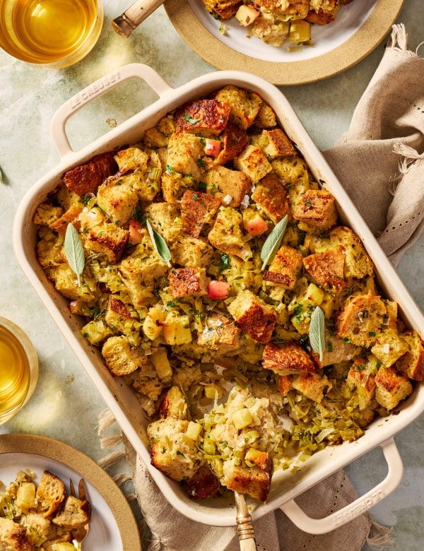 Leak and sage sourdough stuffing baked in a 9x13 casserole dish with spoon scooping out bottom left corner.