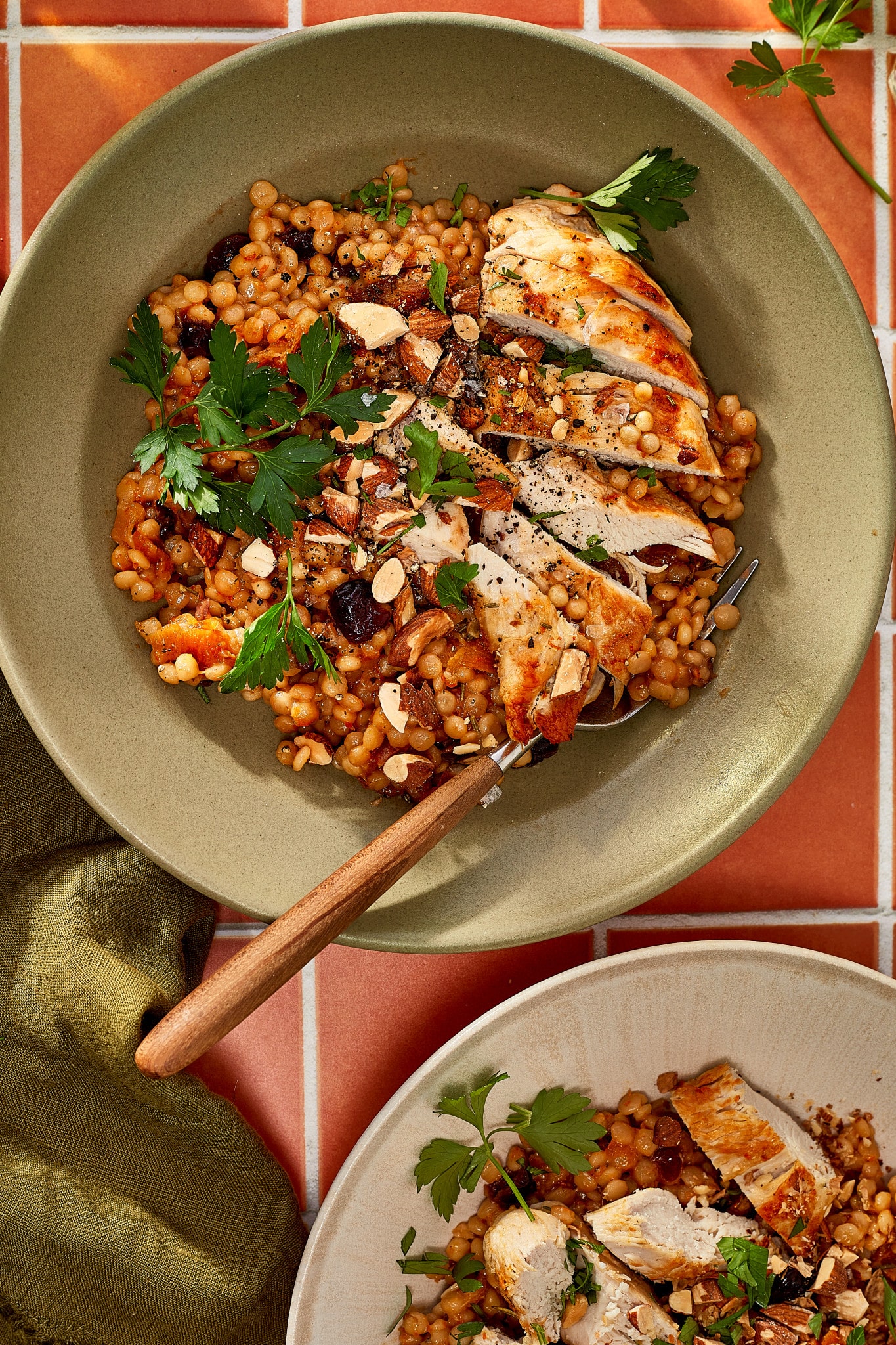 Sliced cranberry apricot chicken served over pearl couscous with dried fruit, chopped almonds, fresh parsley, and black pepper.