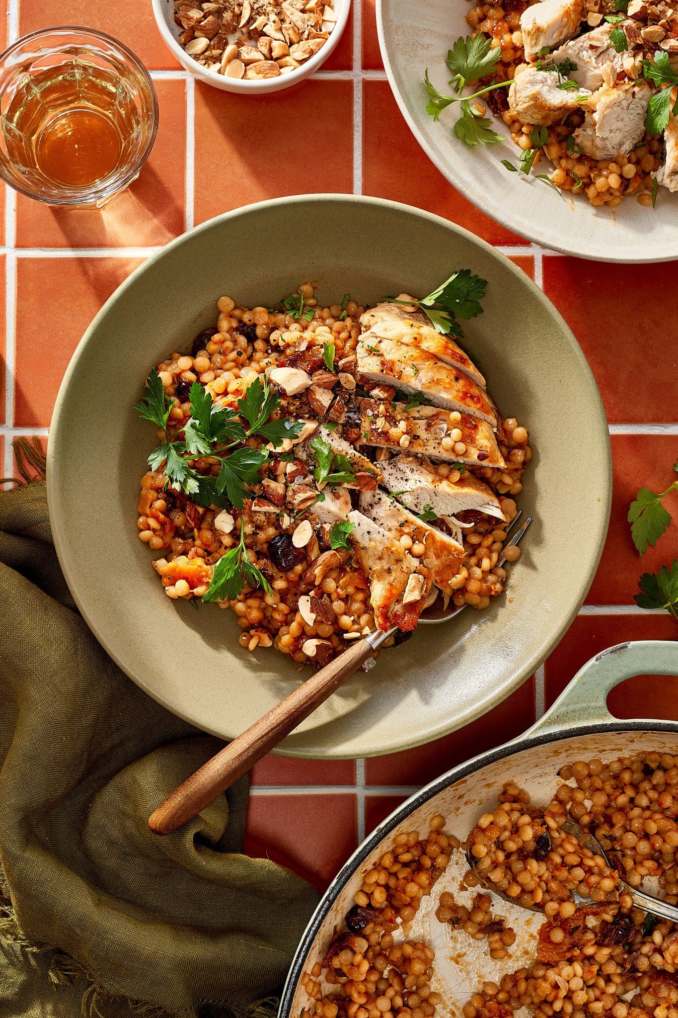Overhead view of cranberry apricot chicken and pearl couscous topped with chopped almonds and fresh parsley, with the skillet alongside.