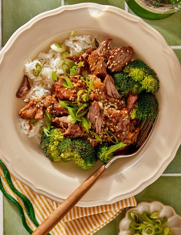 Slow cooker mongolian beef served in a bowl with rice and brococli with a fork on the side.