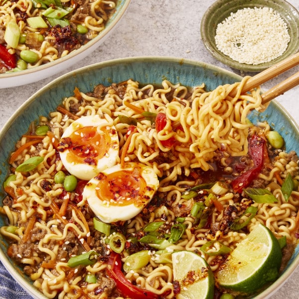 Slow cooker beef ramen served in a bowl topped with toppings and chop sticks picking up a bite of noodles.