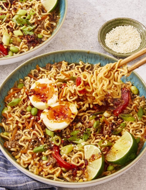 Slow cooker beef ramen served in a bowl topped with toppings and chop sticks picking up a bite of noodles.