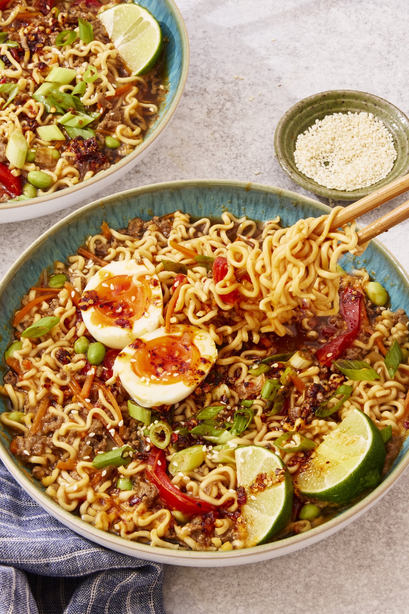 Slow cooker beef ramen served in a bowl topped with toppings and chop sticks picking up a bite of noodles.