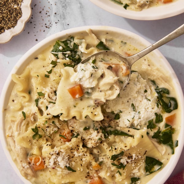 Spoon lifting a bite of white lasagna chicken soup from bowl.