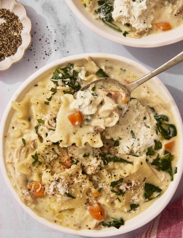 Spoon lifting a bite of white lasagna chicken soup from bowl.
