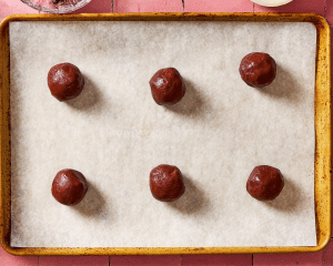 Six balls of cookie dough on a parchment lined baking sheet.