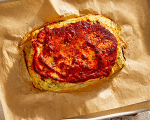 Baked chicken parmesan meatloaf on parchment-lined baking sheet.