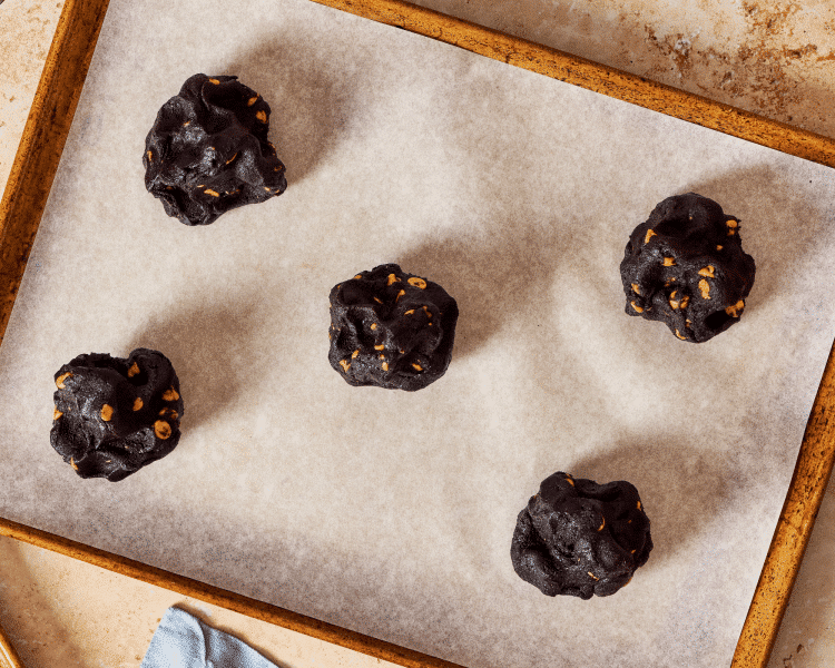 Five mounds of chocolate peanut butter chip cookie dough on parchment lined baking sheet.