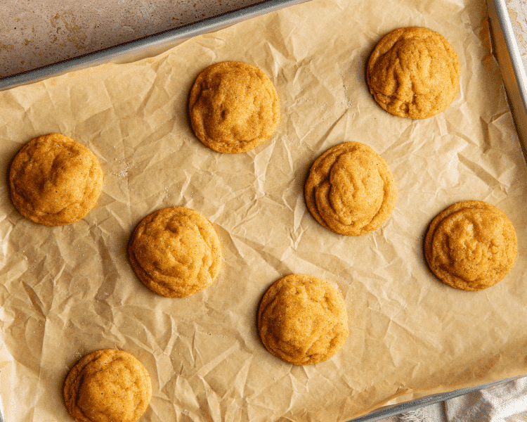Eight pumpkin sugar cookies baked on a parchment-lined baking sheet.
