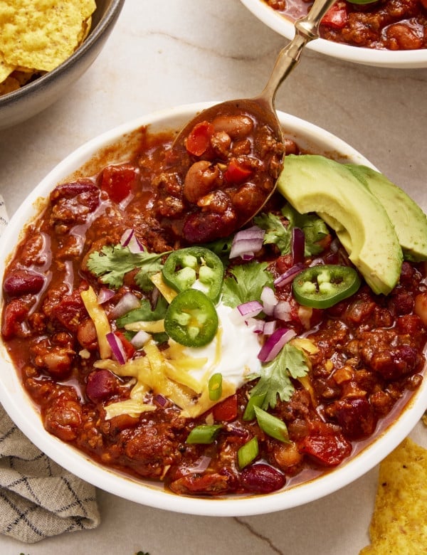 Spoon digging into a bowl of weeknight chili topped with toppings.