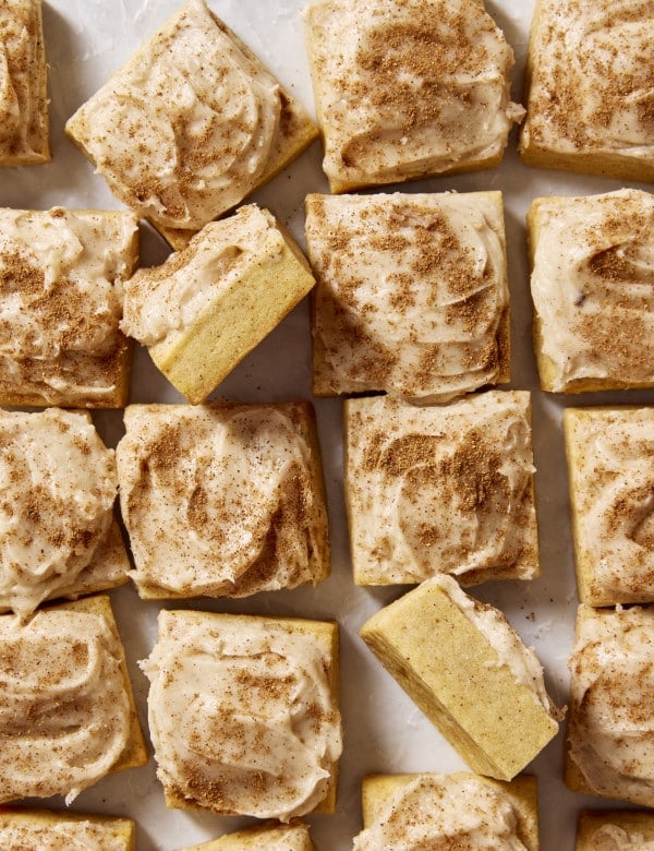 Frosted pumpkin sugar cookie bites cut into squares with two squares turned on their side to show the inside of the cookie.