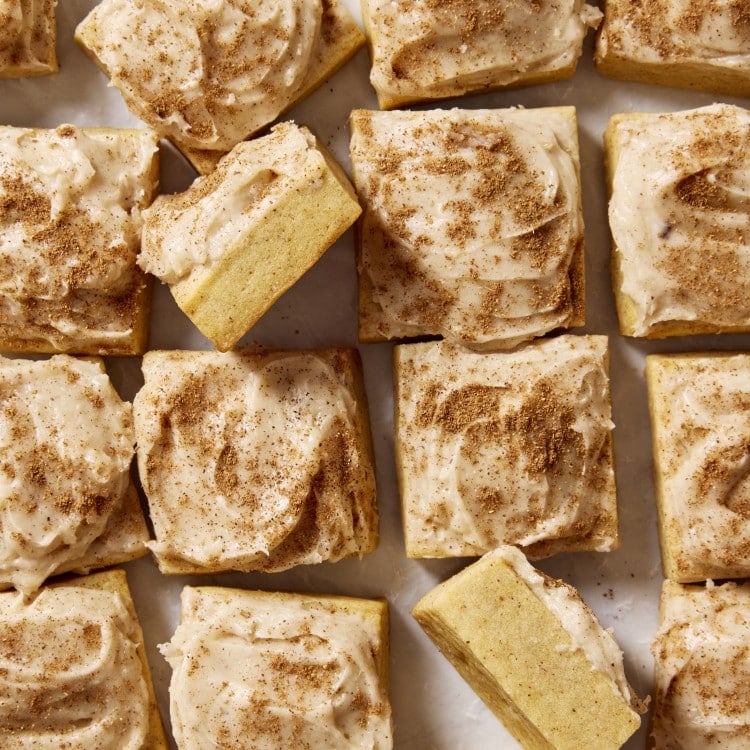 Frosted pumpkin sugar cookie bites cut into squares with two squares turned on their side to show the inside of the cookie.