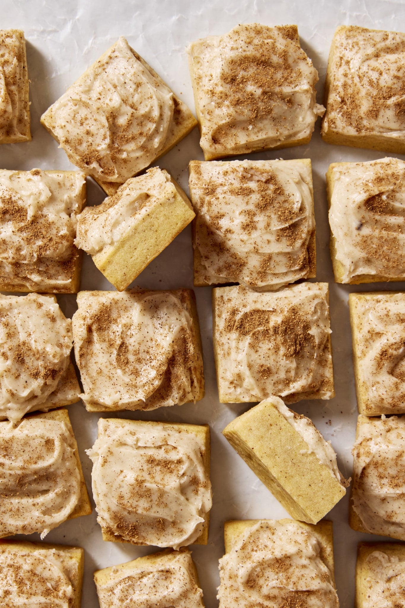 Frosted pumpkin sugar cookie bites cut into squares with two squares turned on their side to show the inside of the cookie.