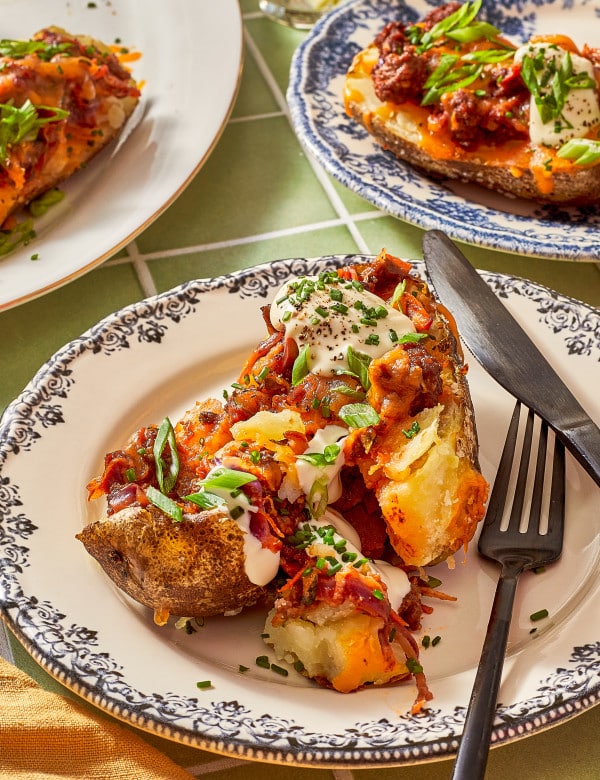 Sloppy joe stuffed baked potato on a plate cut with a fork and knife.