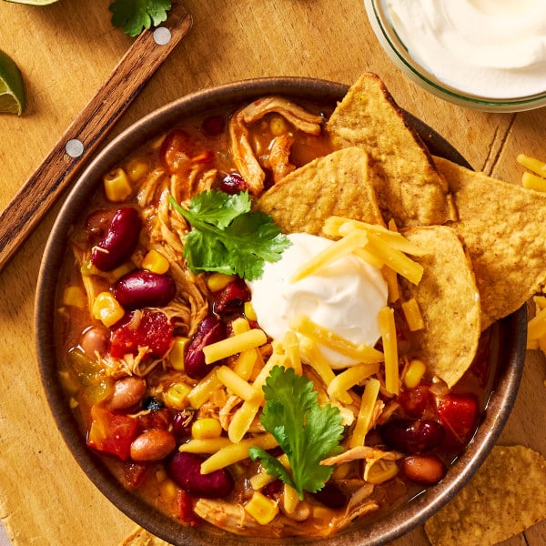 Chicken taco soup served in a bowl with toppings and tortilla chips.