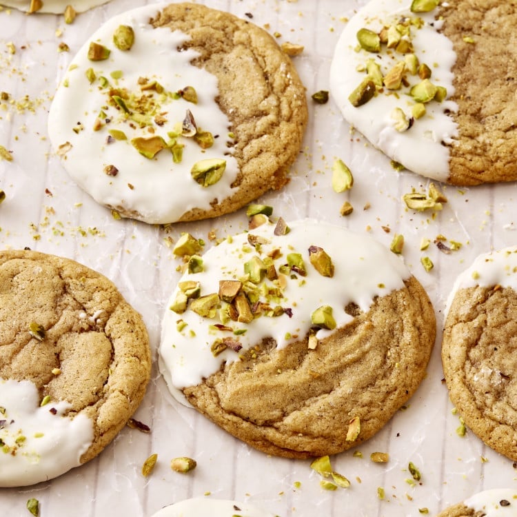 Brown butter sugar cookies dipped in white chocolate and garnished with chopped pistachios on wax paper.