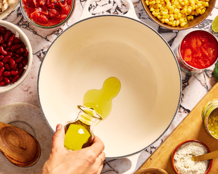 Pouring olive oil in large cast iron pot.